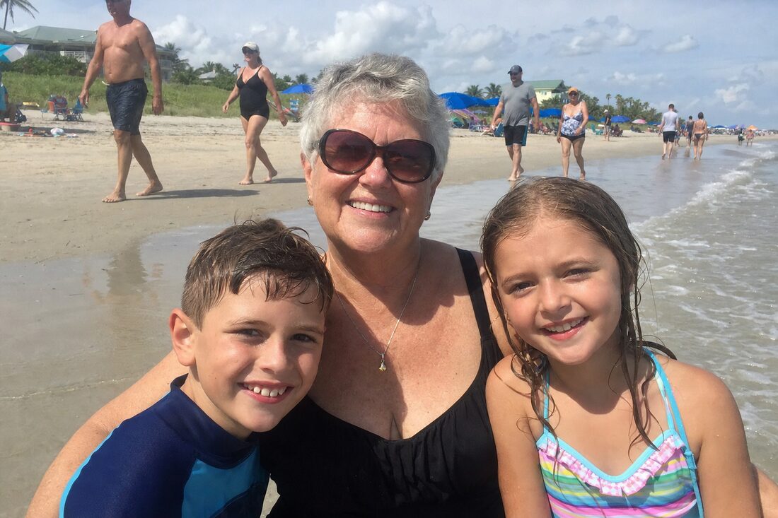 A grandmother and two grandchildren at the beach with strangers in the background